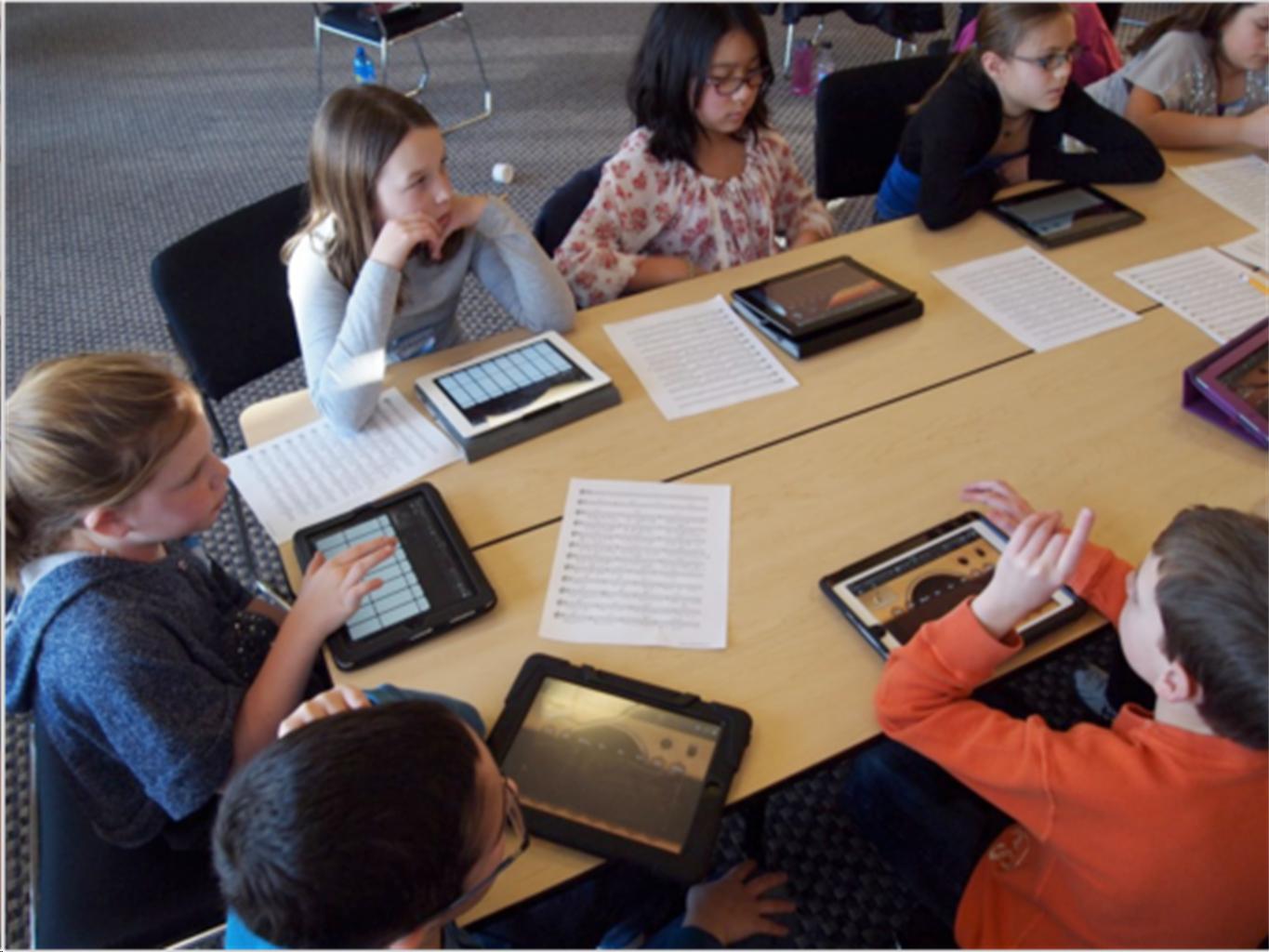 Kids sitting at a table with tablets